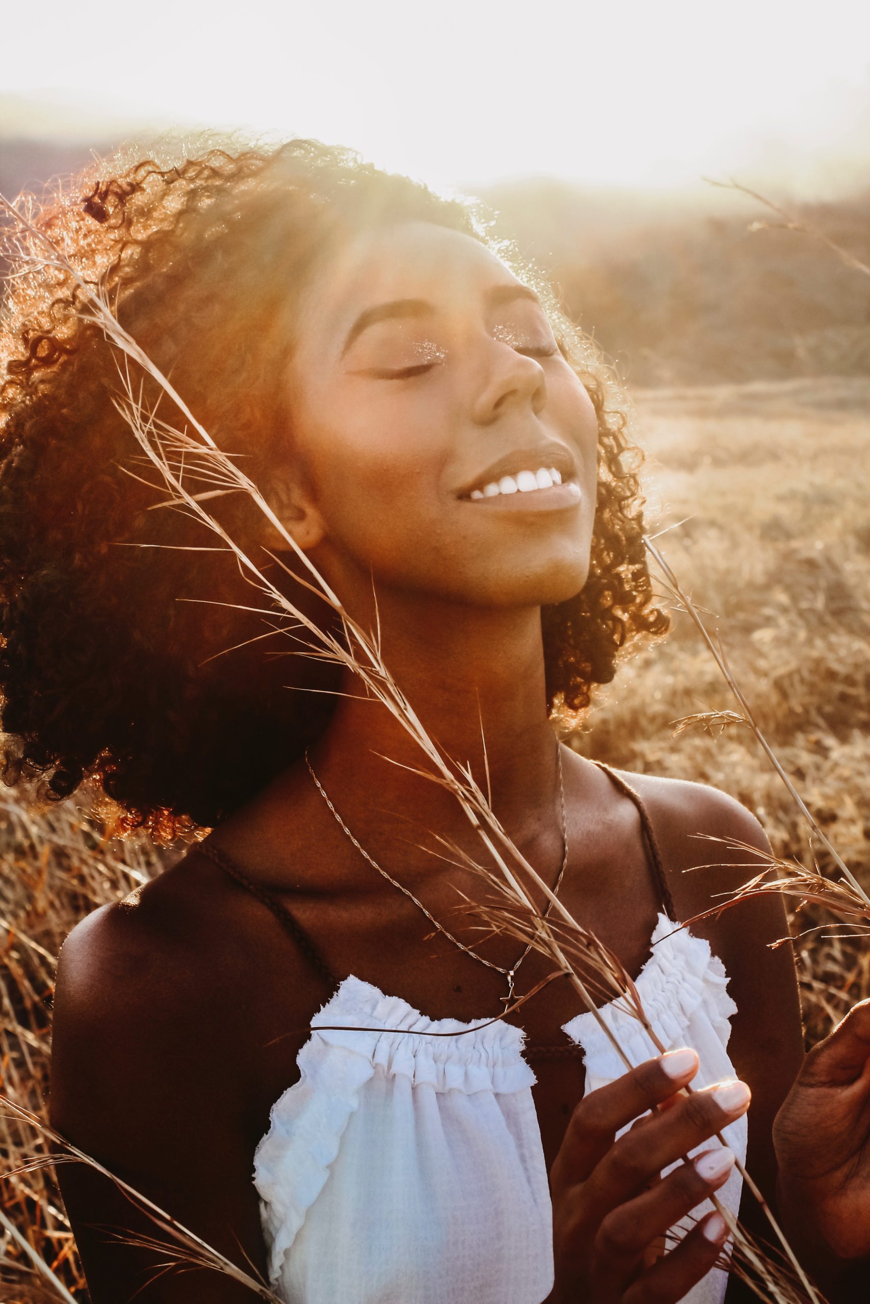 cheerful black woman in field under evening sky featured image for 5 Tips for Feeling Empowered and Motivated for the New Year by Koya Webb